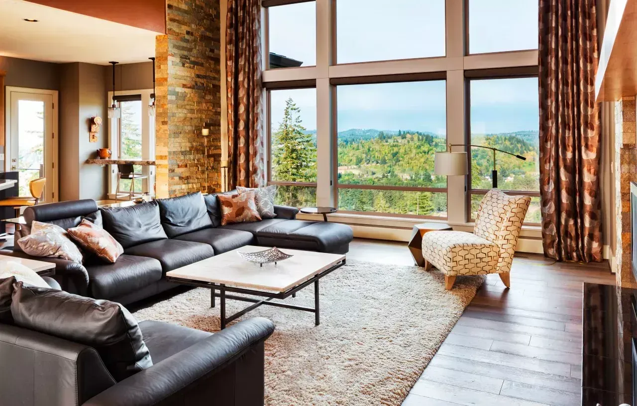 Modern living room with leather sectional, patterned chair, large windows, and mountain view