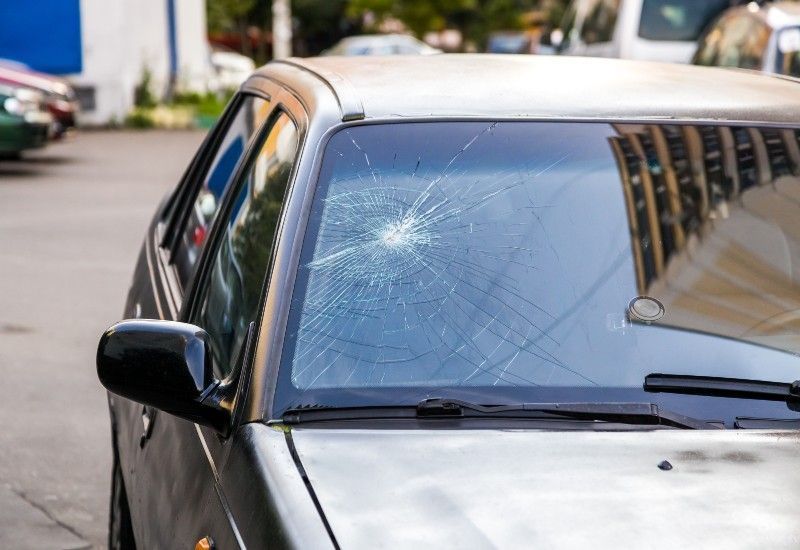 Car windshield with a spiderweb crack from impact, parked on a street