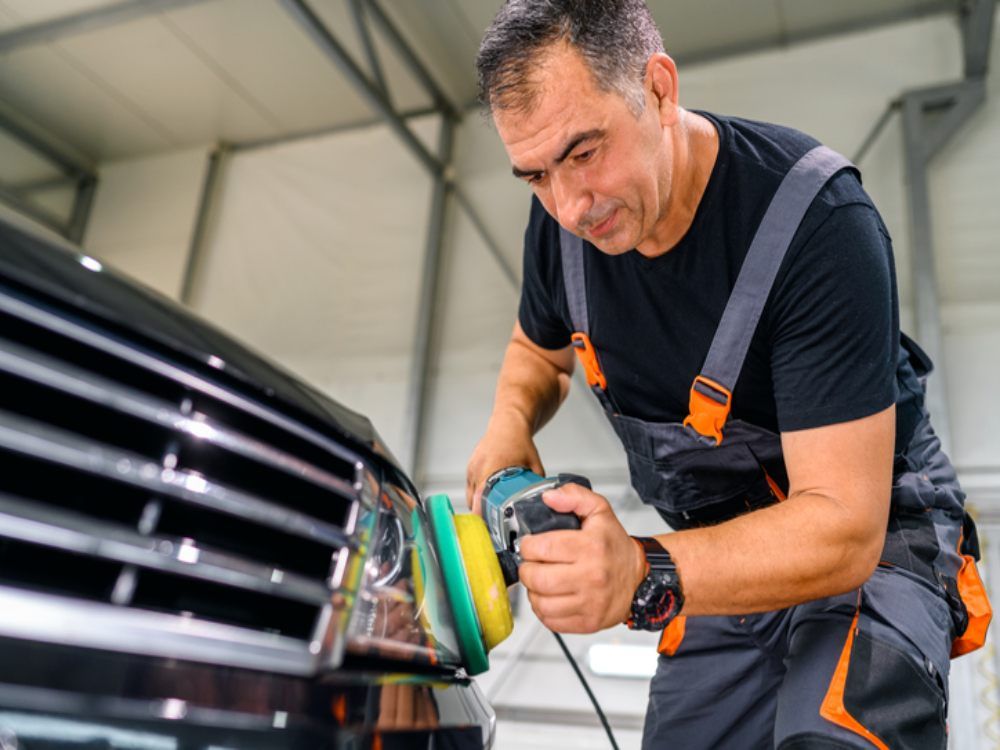 Mechanic polishing a car grille with a power buffer in a garage