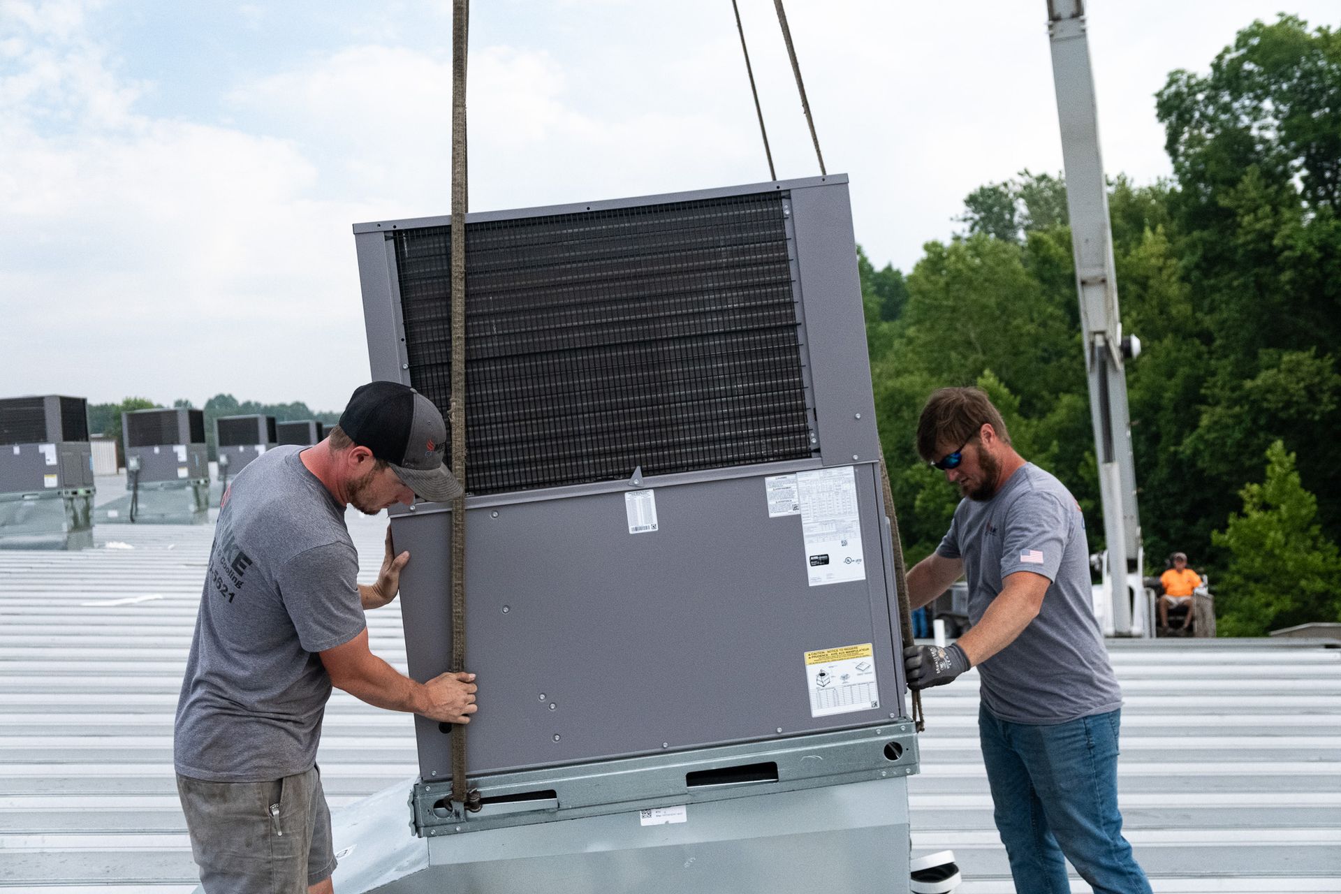 Two Men Are Lifting a Large Box on Top of A Roof | Union, MO | Menke Heating and Cooling