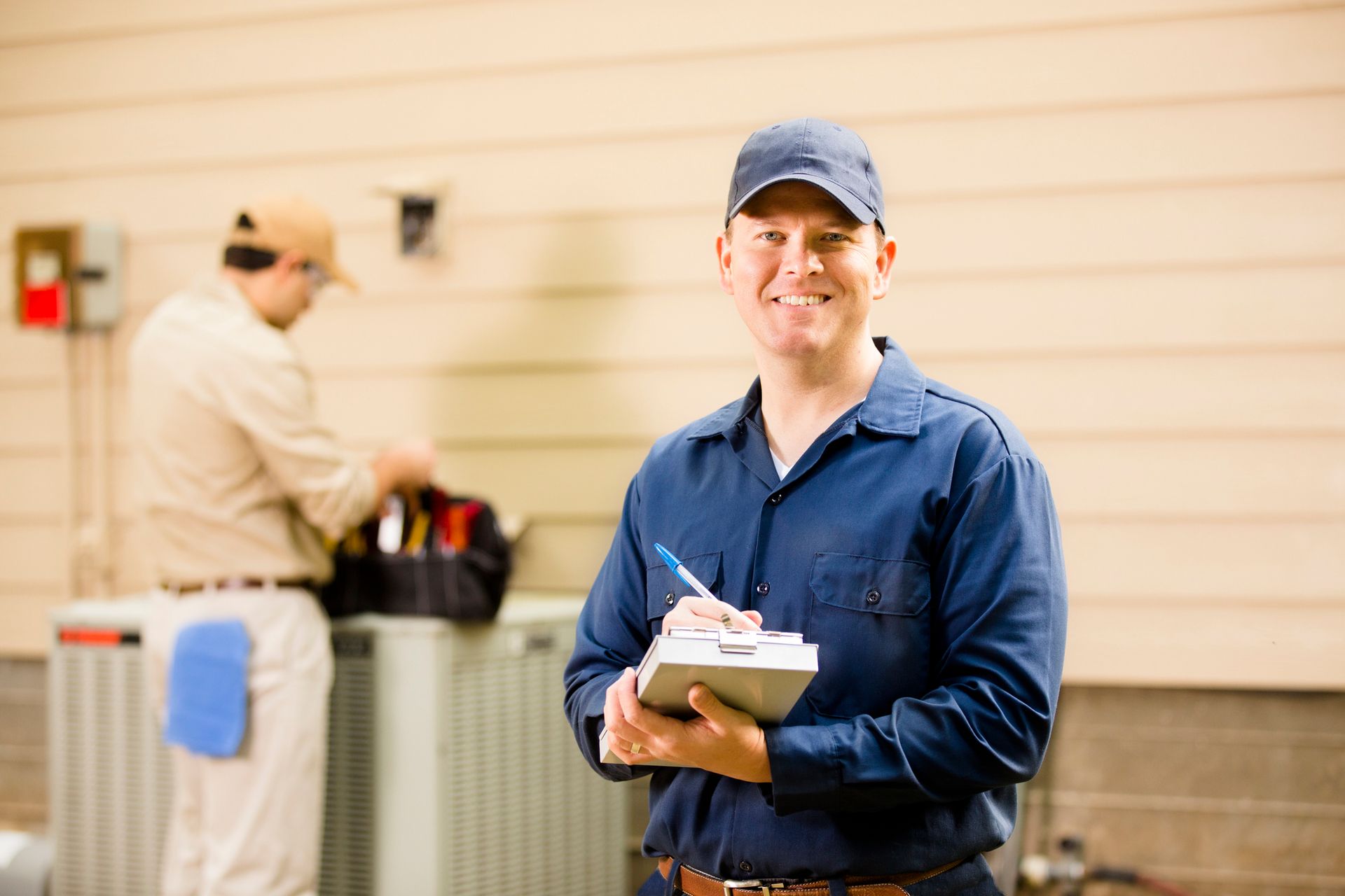 A Caucasian and Latino repairman team up to fix a home's air conditioner outdoors | Washington, MO