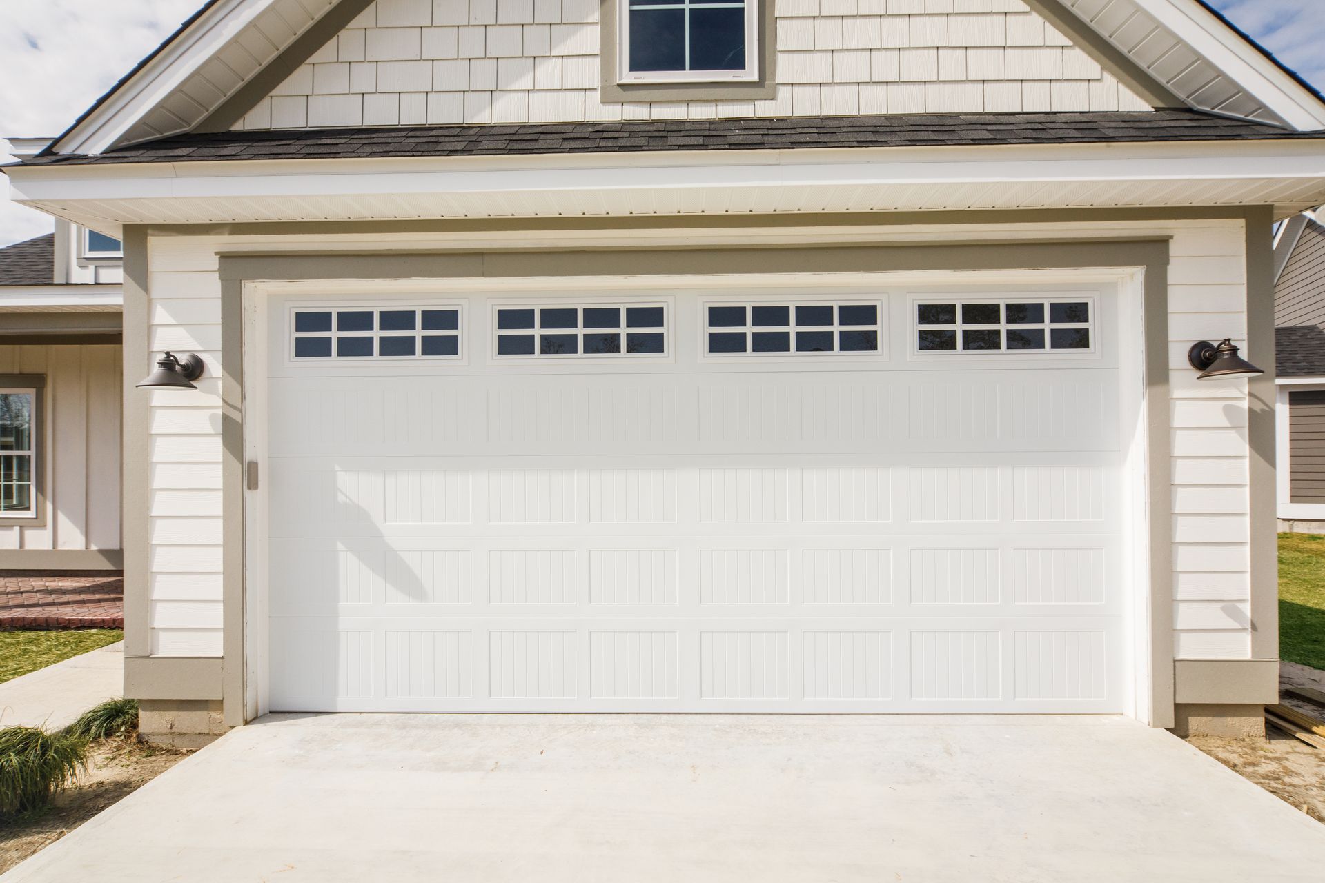 A white garage door is sitting in front of a white house.