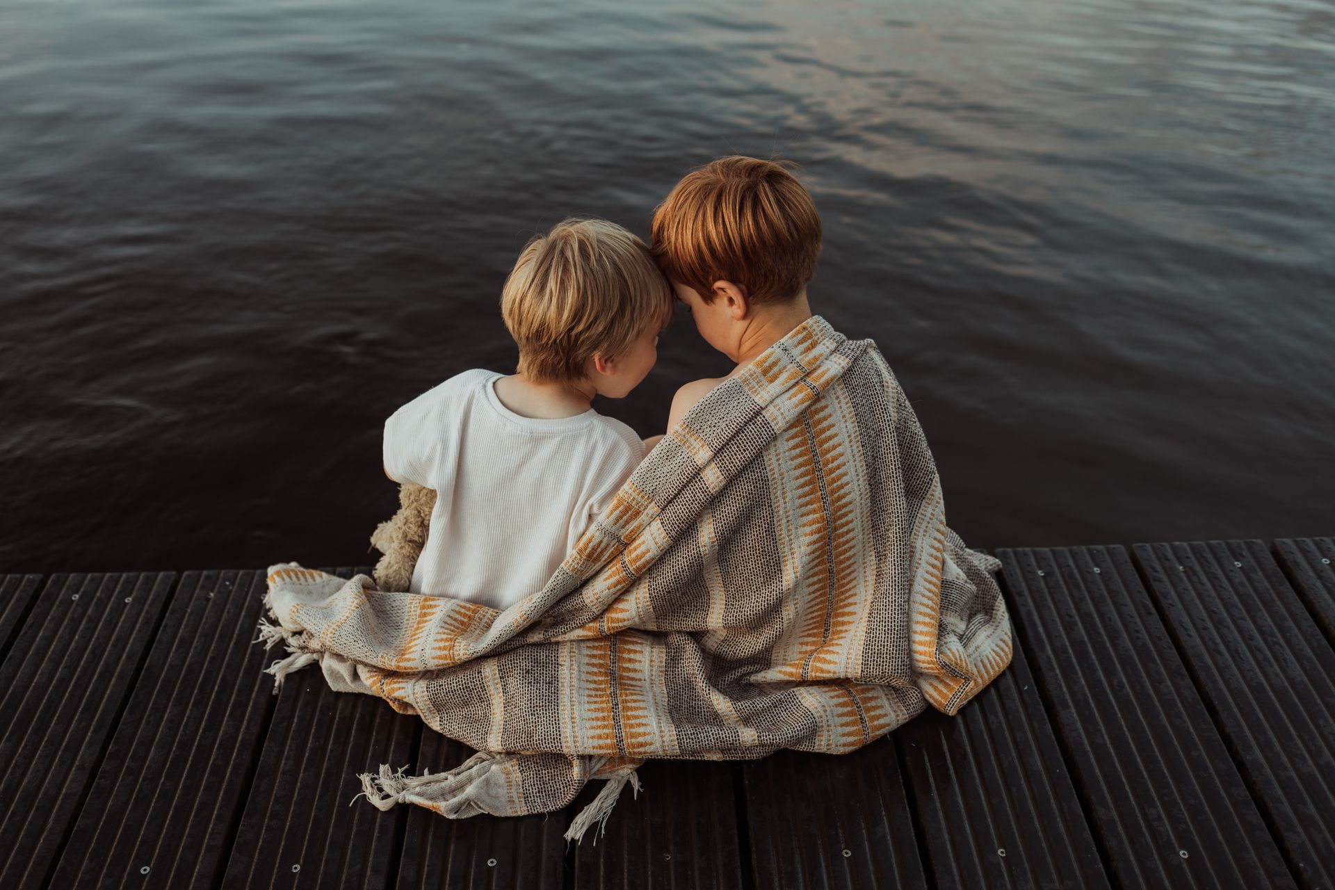 Broertjes Twee jonge jongens, knus gewikkeld in een deken, zitten op een steiger aan het water