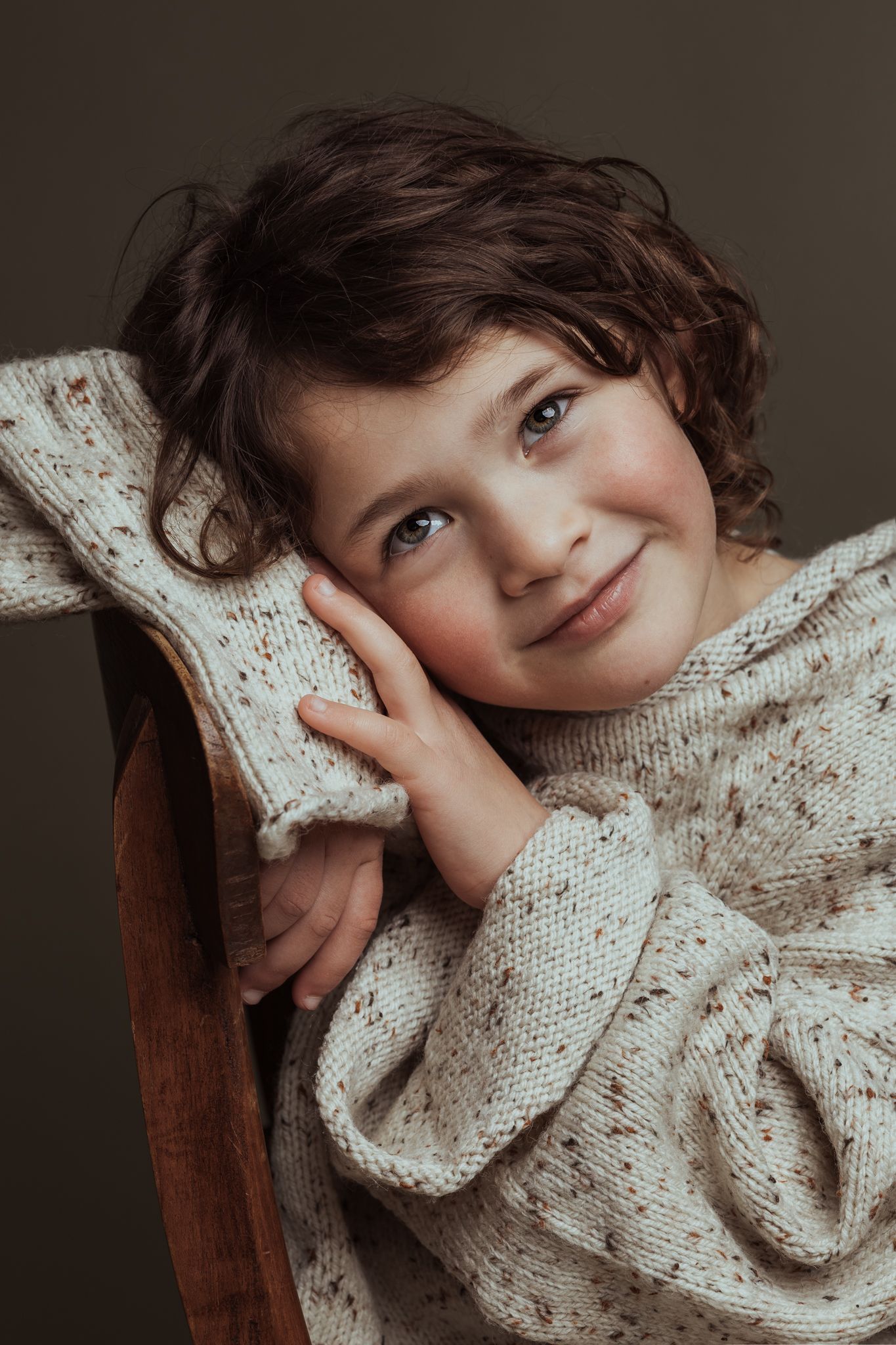 Dromerig kinderportret van een meisje dat leunt tegen een stoelleuning in een fotostudio in Amersfoort.