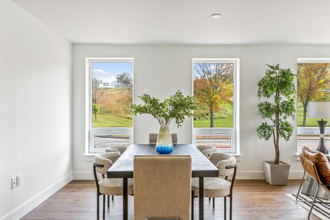 Bright dining room with a wooden table, beige chairs, and large windows overlooking greenery