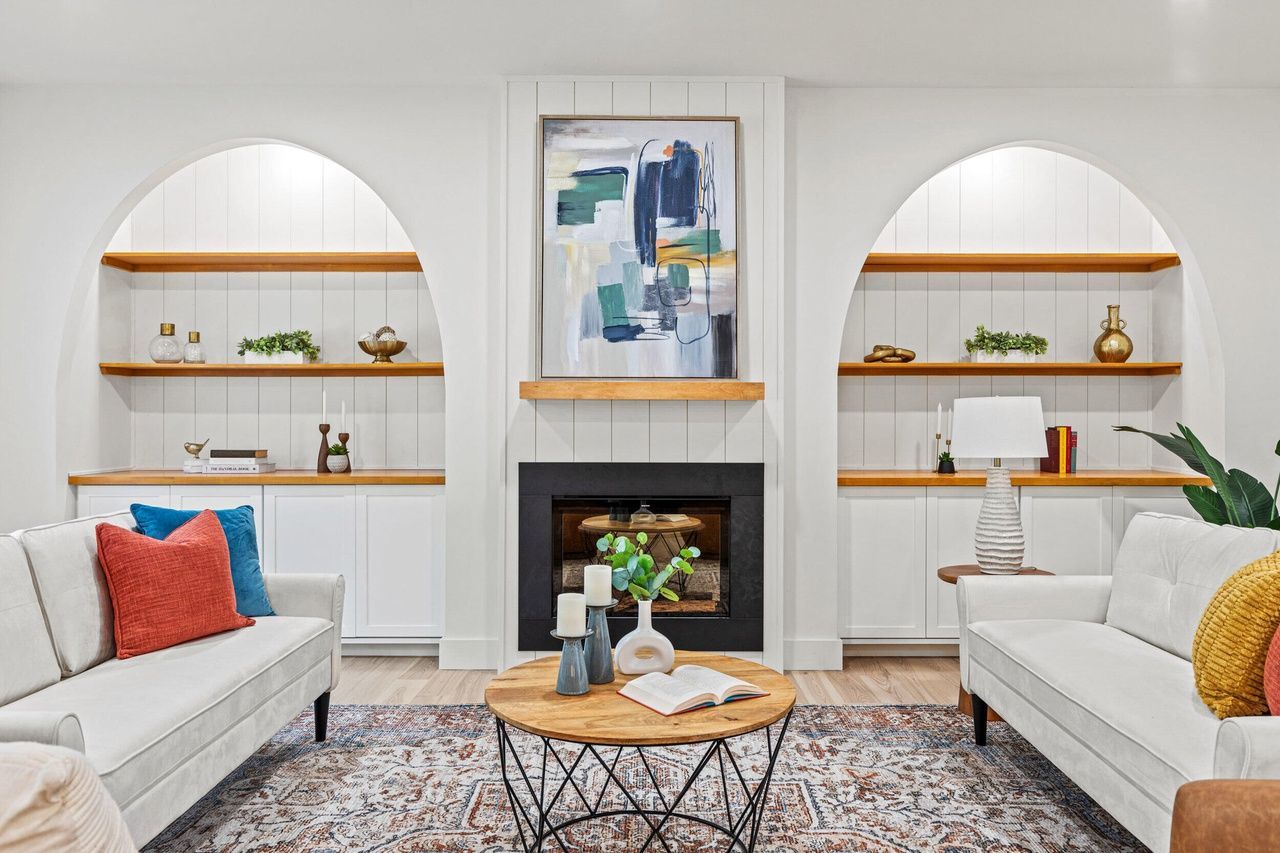 Sunlit living room with two chairs, blue rug, framed art, and decorative candles on a dark wood floor.