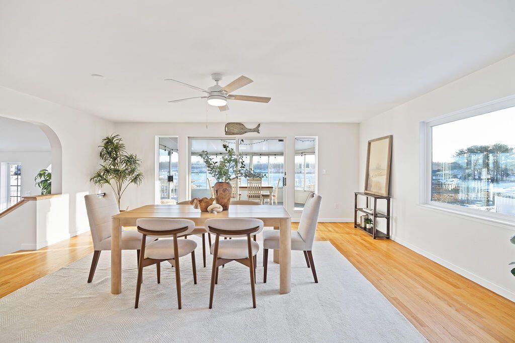 Bright living room with white and green furniture, wood floors, and a large window with plants