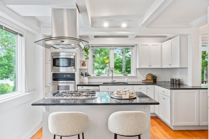 Bright modern white kitchen with a black island, built-in oven, and large windows over a sink