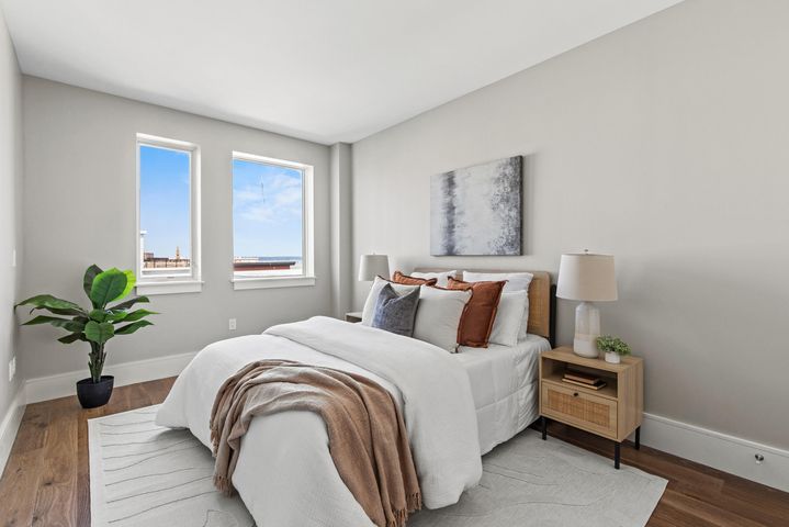 Bright bedroom with white bed, wooden nightstands, plant, and two windows letting in natural light
