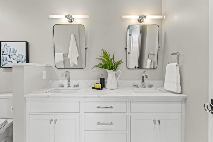 Bright white bathroom vanity with double sinks, mirrors, wall lights, and green plant decor
