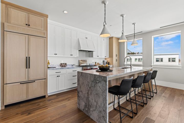 Modern kitchen with white cabinets, marble island, bar stools, and large windows overlooking a bright neighborhood