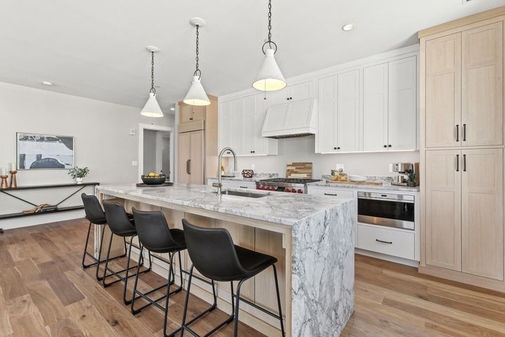 Modern kitchen with white cabinets, marble island, black stools, and pendant lights