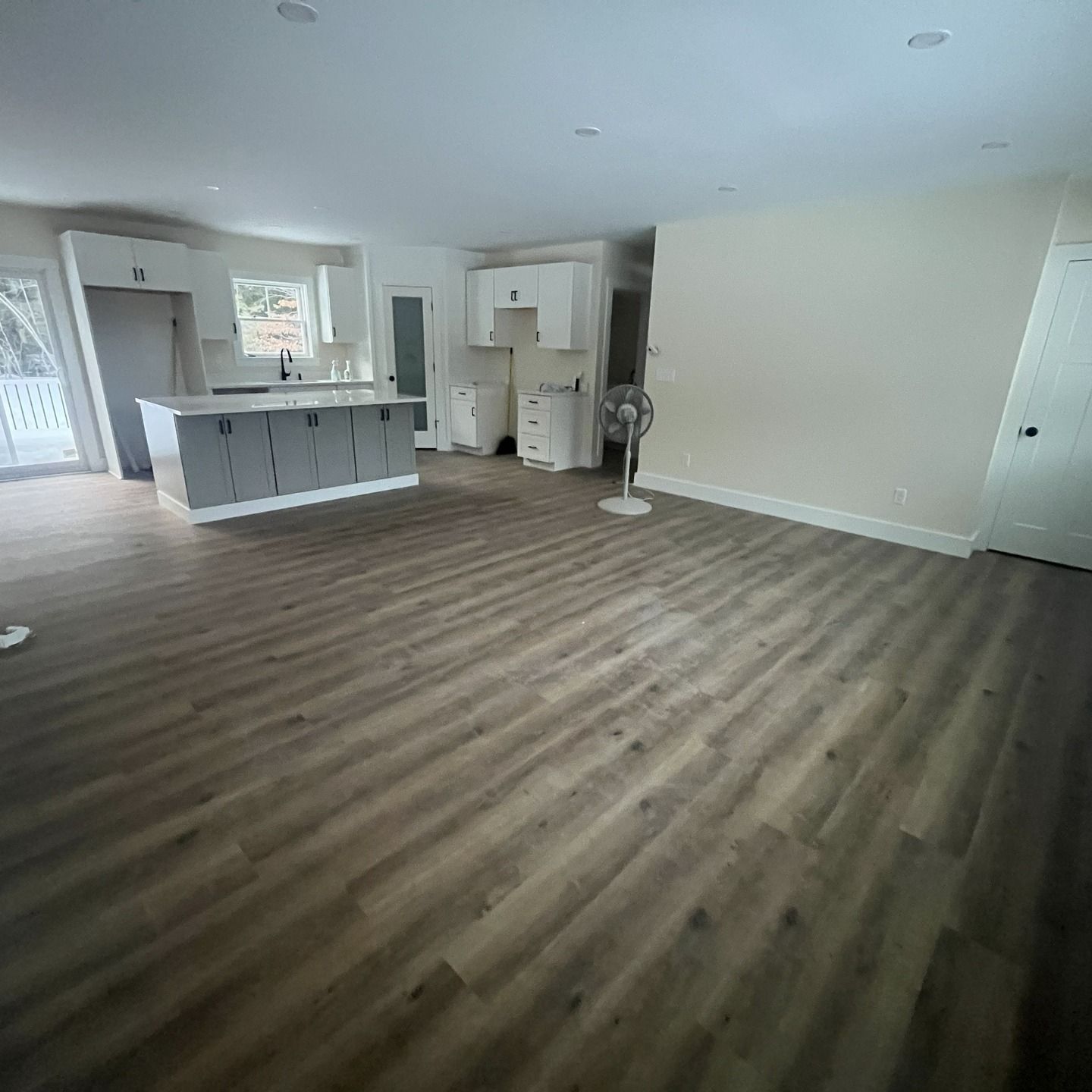 Empty open-plan living room with wood-look floors, white walls, and a kitchen island in the background