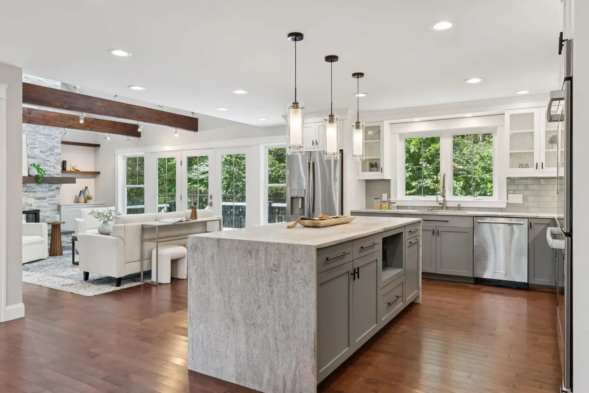 Bright open kitchen with a large island, stainless appliances, white cabinetry, and an adjoining living area