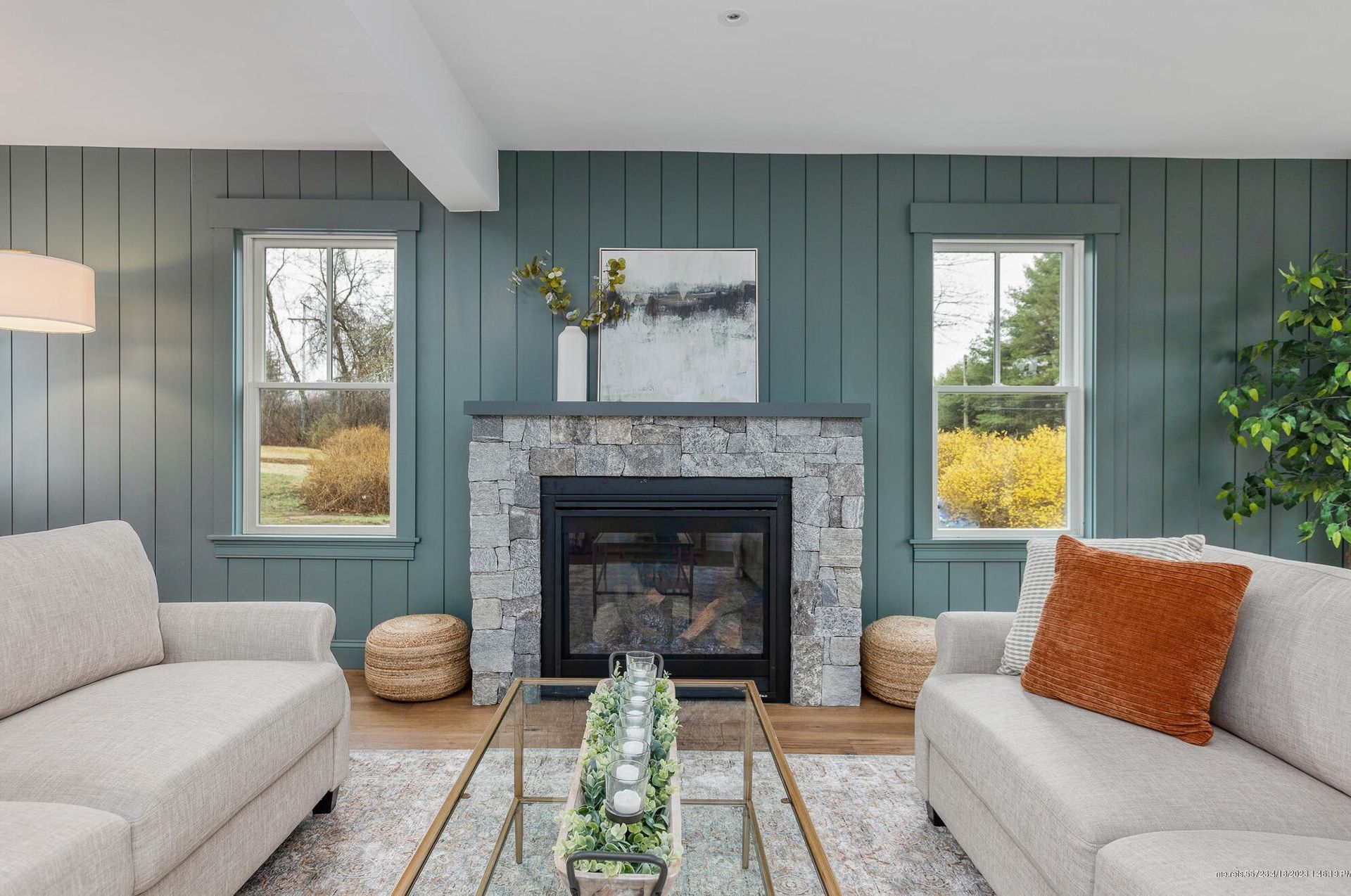 Cozy living room with gray fireplace, sage paneled walls, beige sofa, and orange accent pillow