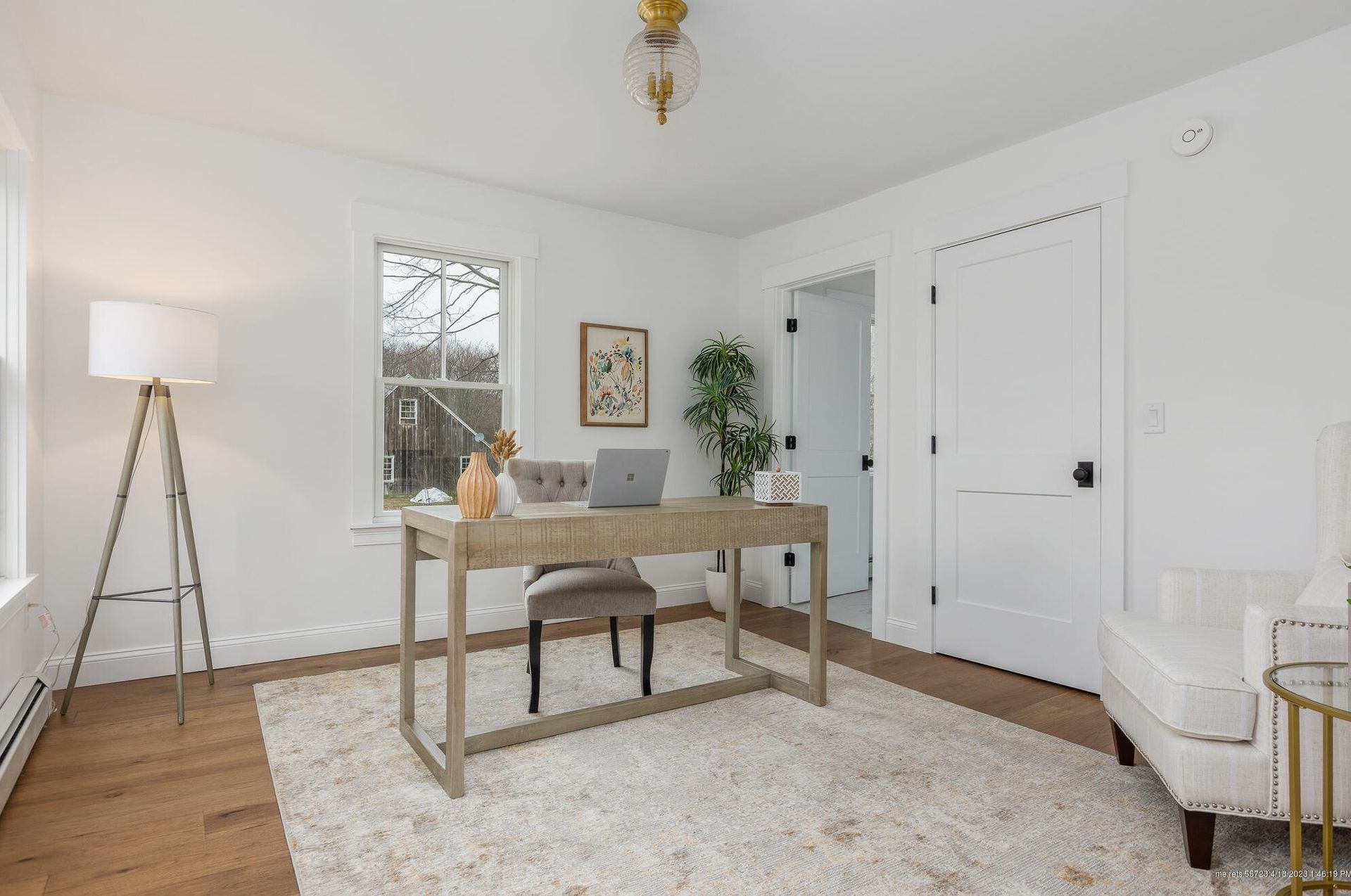 Bright home office with a wooden desk, chair, lamp, rug, and white walls.