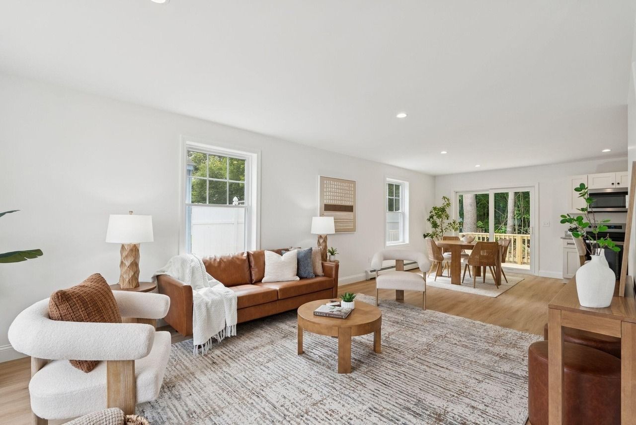 Bright modern living room with white walls, tan sofa, chairs, rug, and dining area beyond