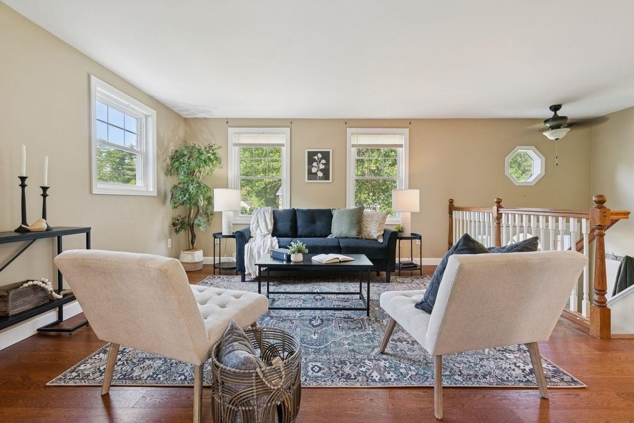Bright living room with blue sofa, beige chairs, patterned rug, and windows letting in natural light