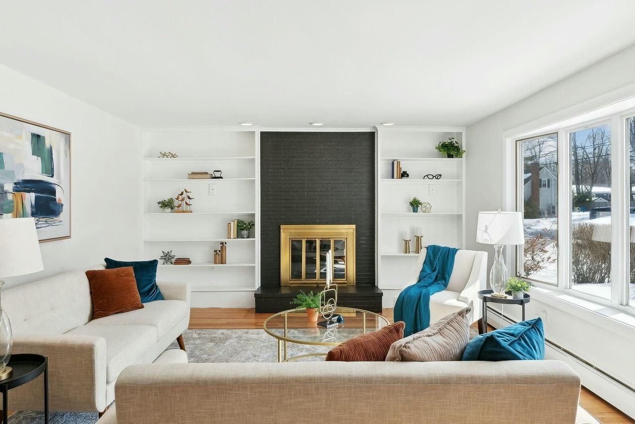 Bright living room with a fireplace, white walls, large windows, and teal and orange accents