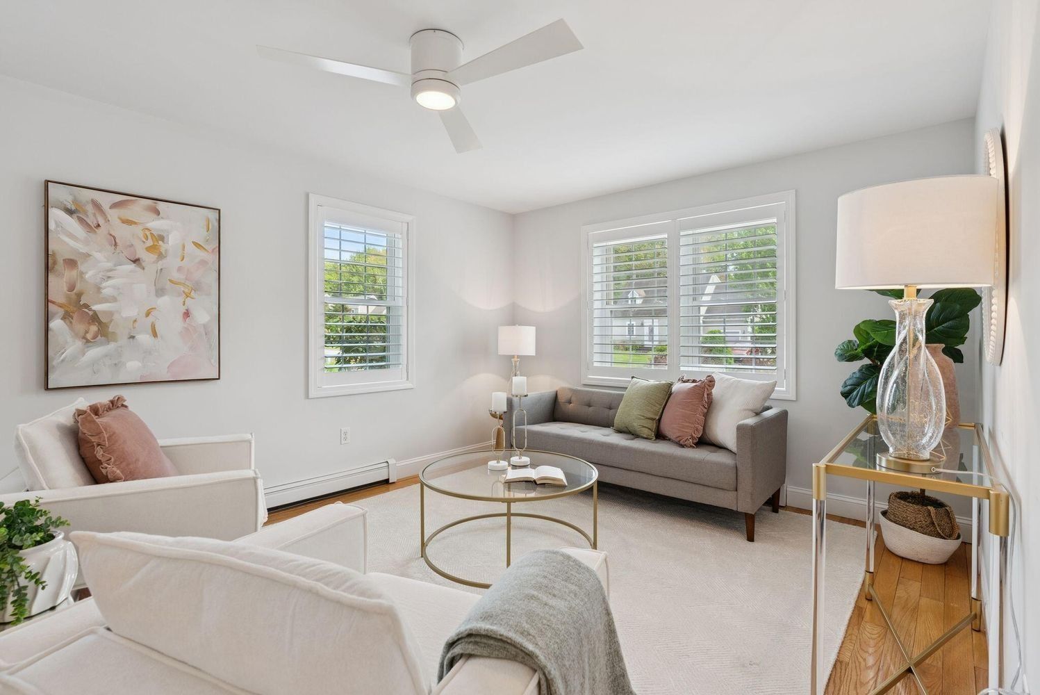 Bright, airy living room with white chairs, gray sofa, round coffee table, and large windows with shutters