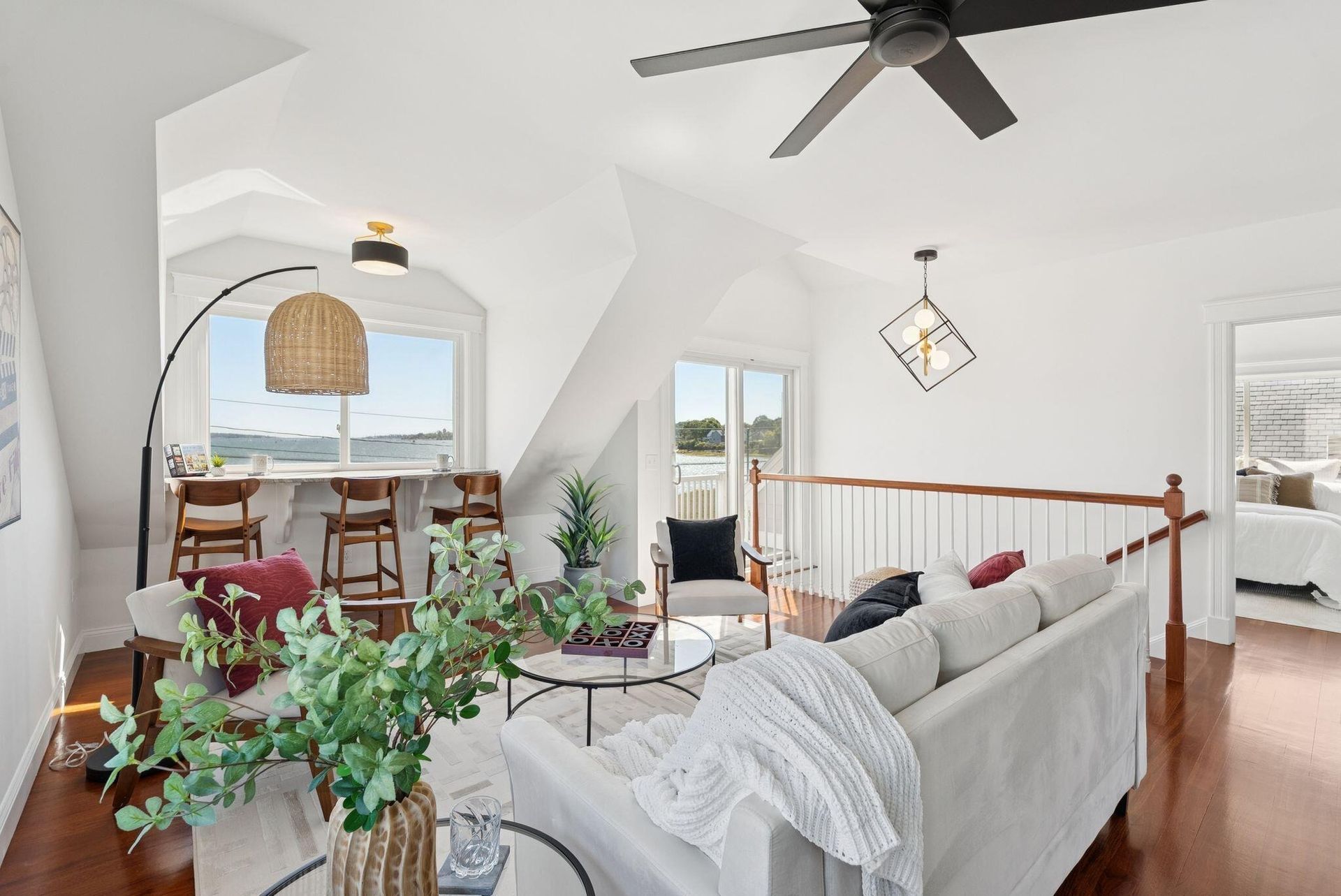 Bright living room with gray sofa, dining nook, arched window, and ceiling fan in a white home interior
