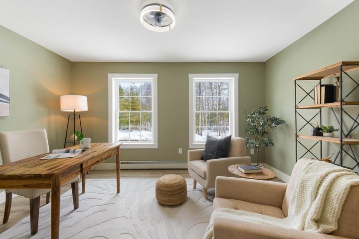 Bright home office with wooden desk, beige sofa, two windows, and soft green walls