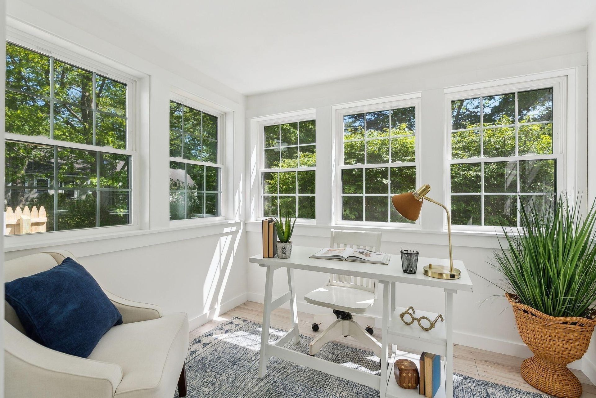 Bright white home office with desk, chair, windows, plants, and blue accent pillow in a sunlit room