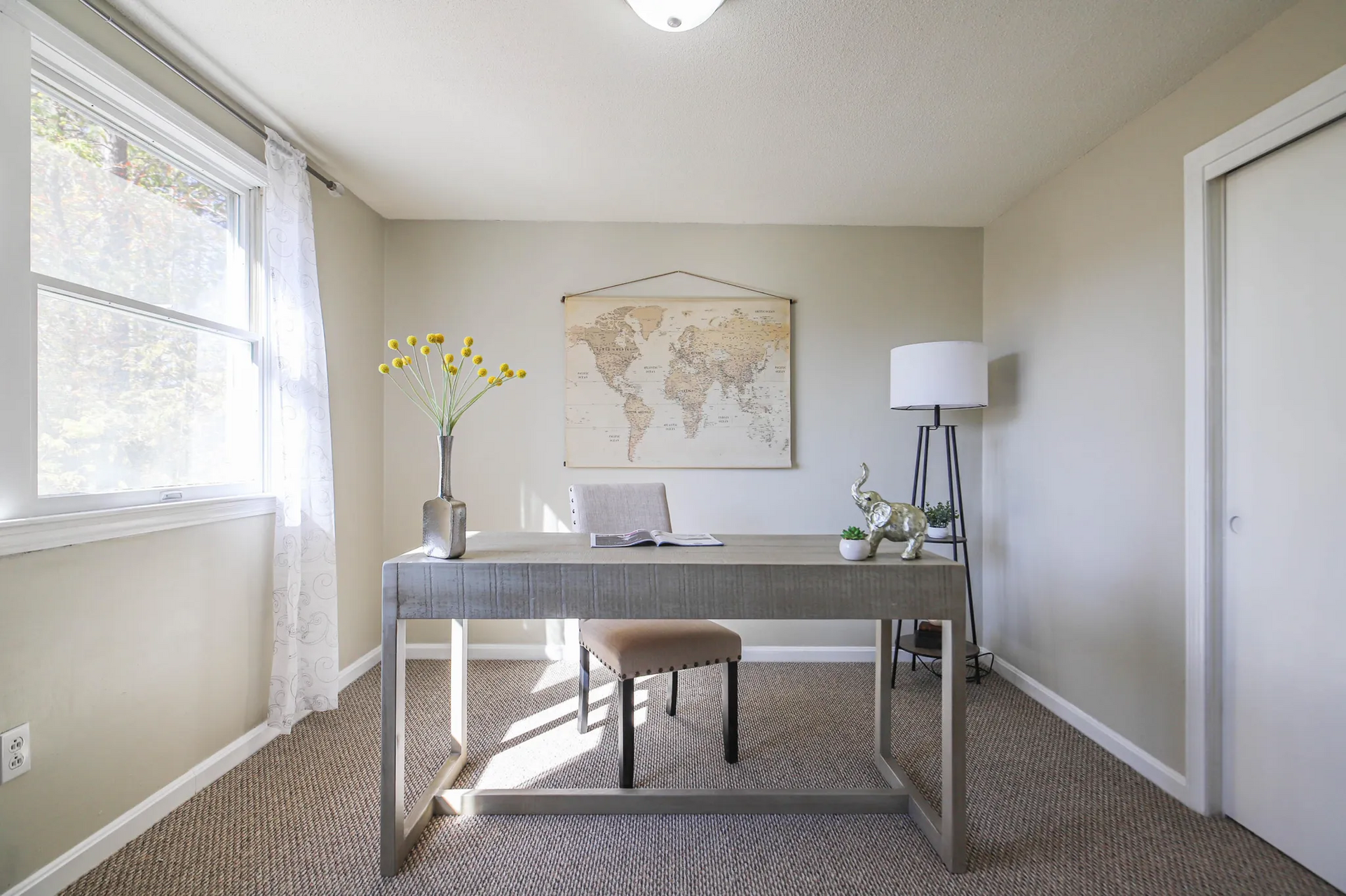 Bright home office with desk, laptop, lamp, chair, wall art, and a window on the left