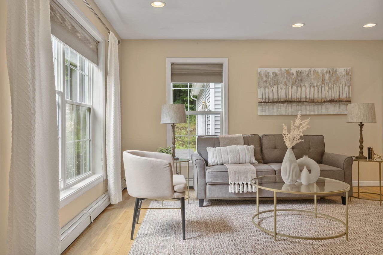 Bright living room with gray sofa, white chairs, round coffee table, and large windows, in soft beige tones