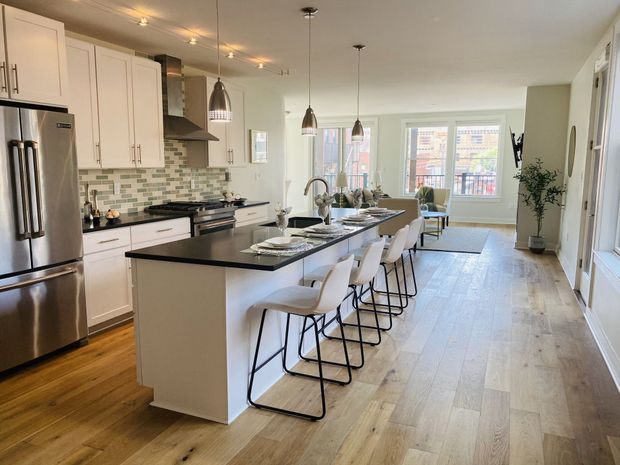 Bright modern kitchen with island, bar stools, stainless appliances, and dining area by large windows.