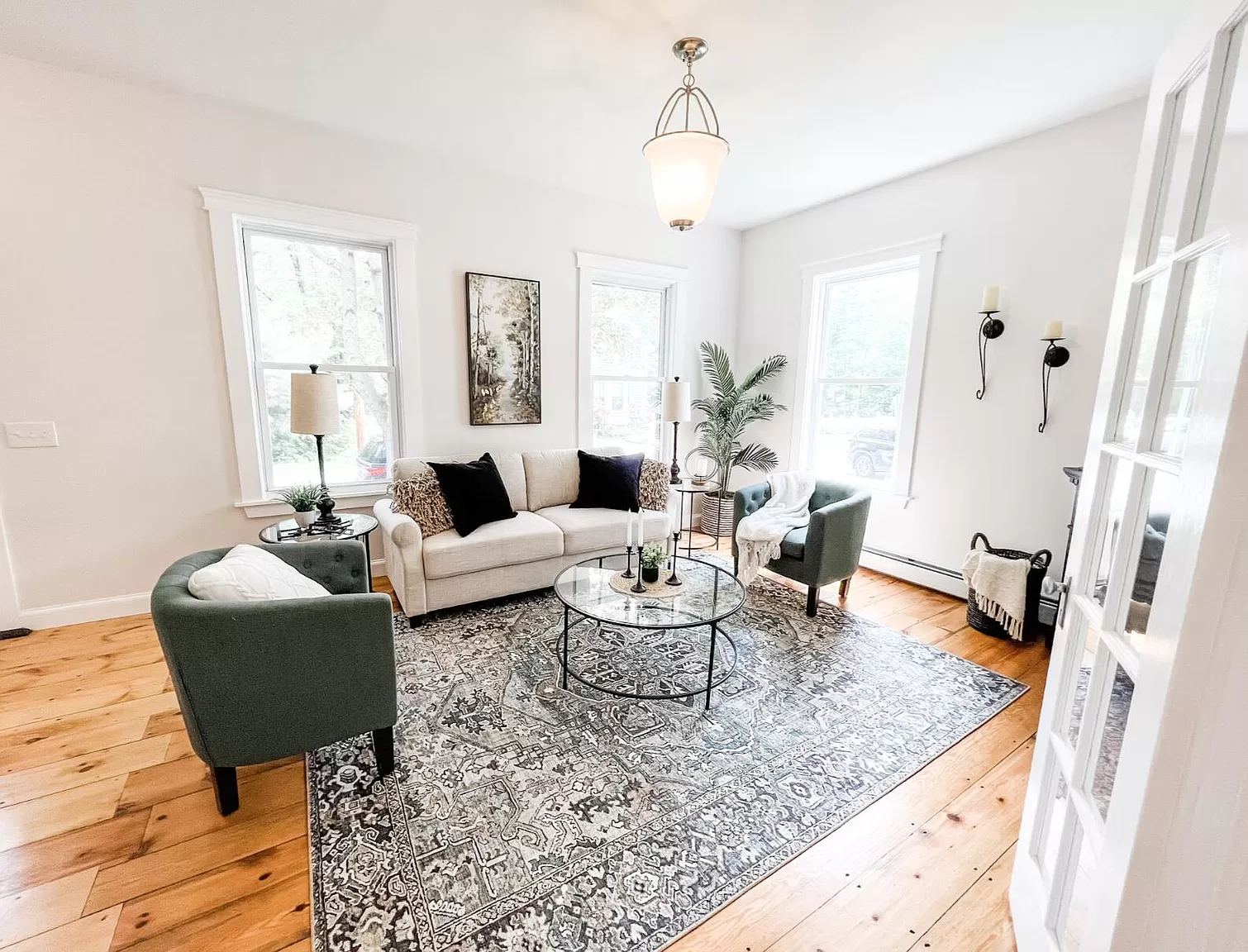 Bright living room with white walls, gray sofa, green chairs, a patterned rug, and wooden floors