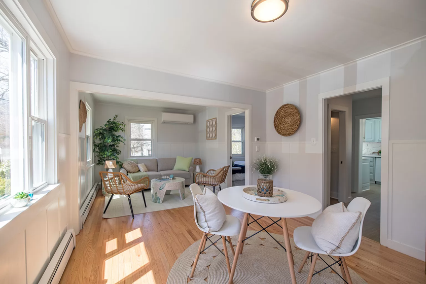 Bright, airy living-dining room with white walls, wood floors, round table, chairs, sofa, and large windows.