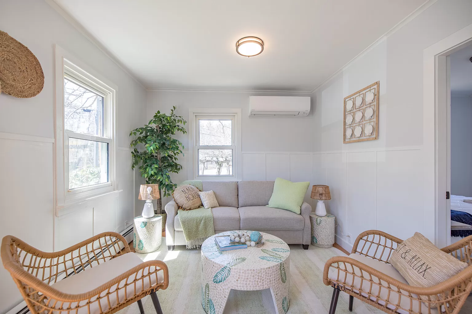 Bright sunroom with gray sofa, wicker chairs, patterned rug, and potted plant in soft neutral tones