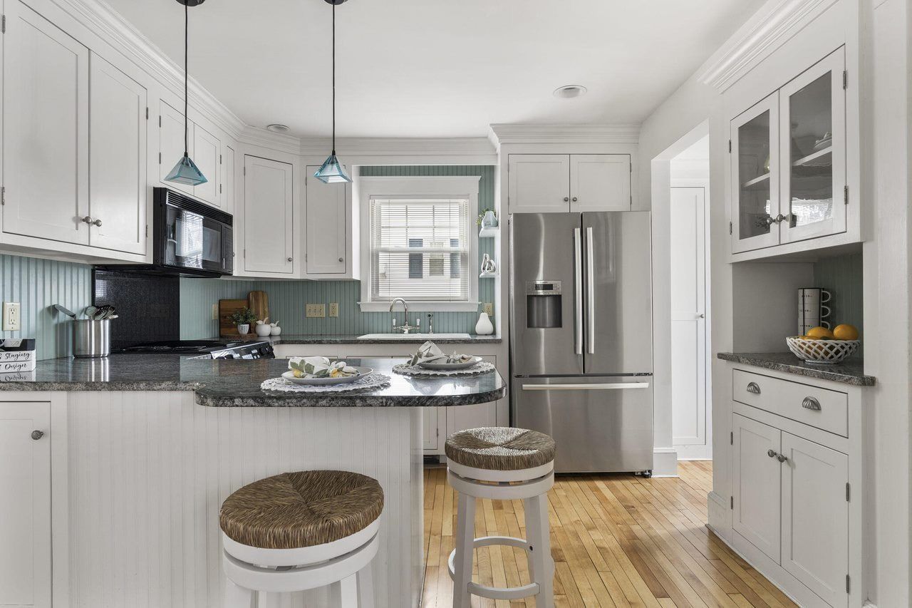 Bright white kitchen with stainless steel appliances, marble island, and bar stools.
