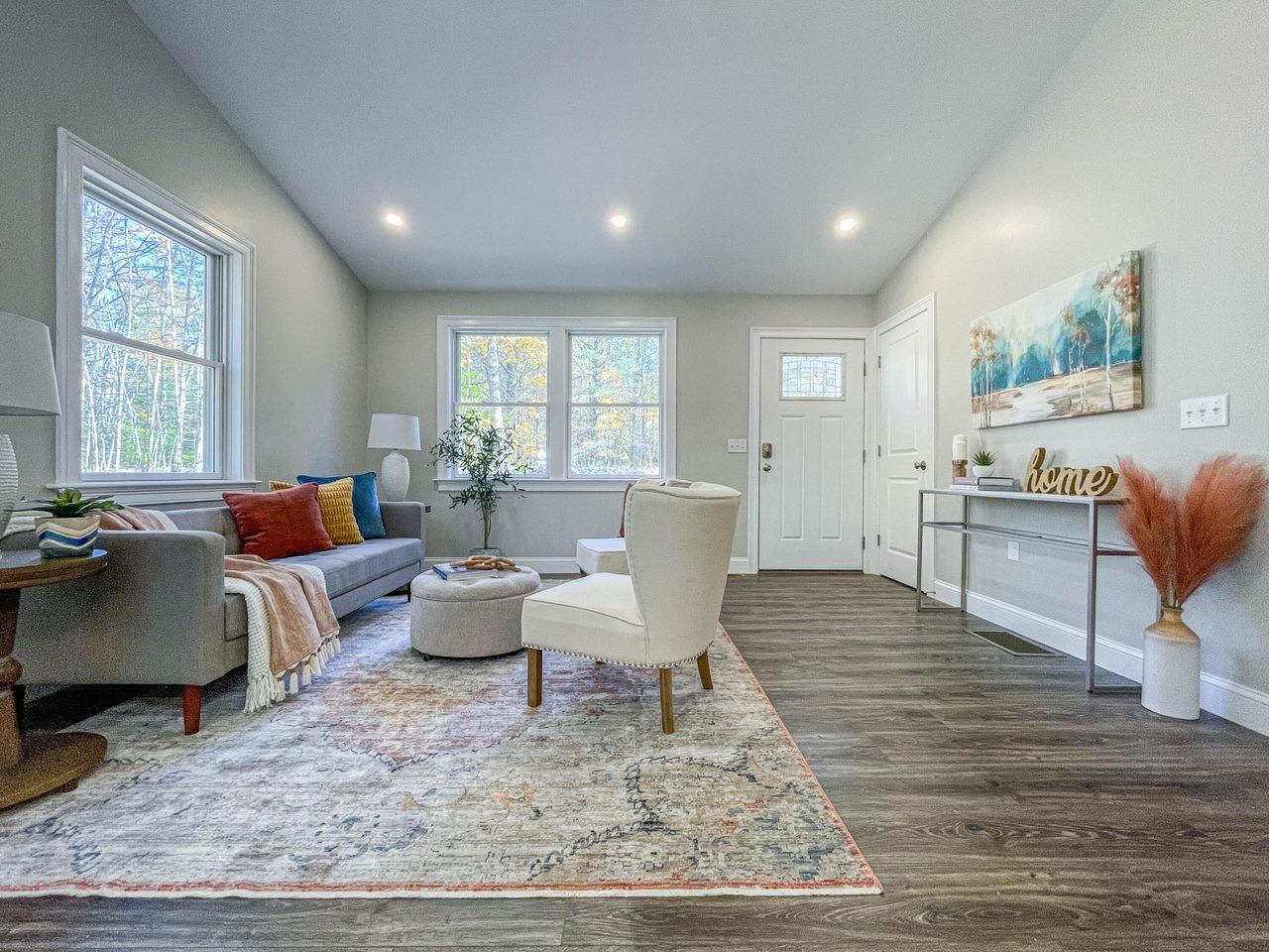 Bright modern living room with gray sofa, cream chairs, rug, white walls, and wood flooring