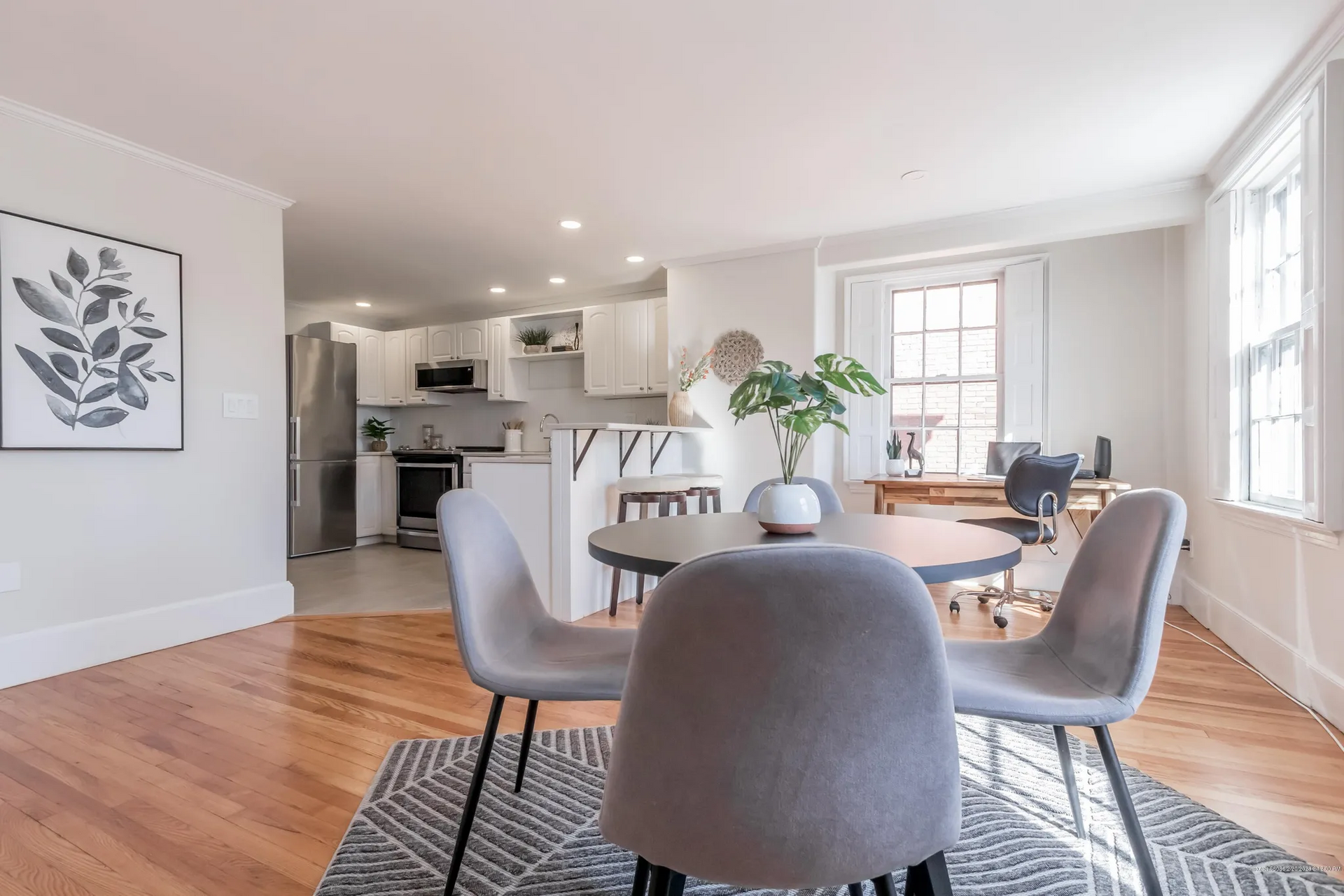 Bright open dining room with round table, gray chairs, hardwood floors, and a kitchen in the background