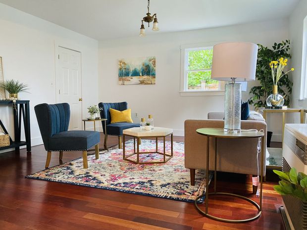 Bright living room with blue chairs, round coffee table, patterned rug, and a floor lamp by the window.
