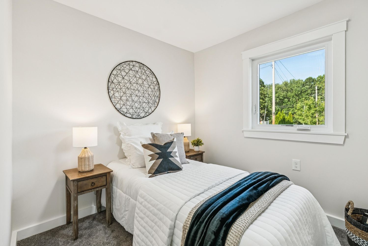 Bright bedroom with a white bed, gray walls, bedside table, wall art, and a window view of greenery