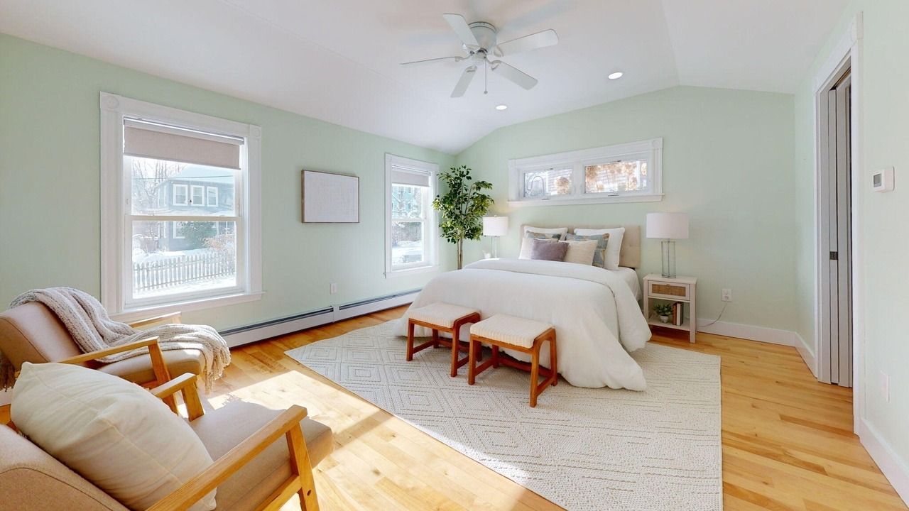Bright bedroom with white bed, wood floors, mint walls, and seating by the window