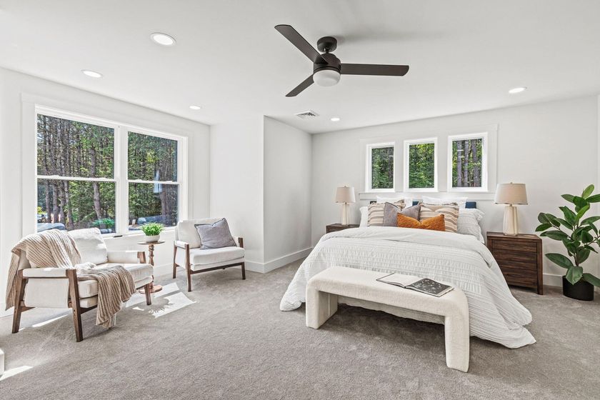 Bright, airy bedroom with a bed, armchairs, large windows, and a ceiling fan