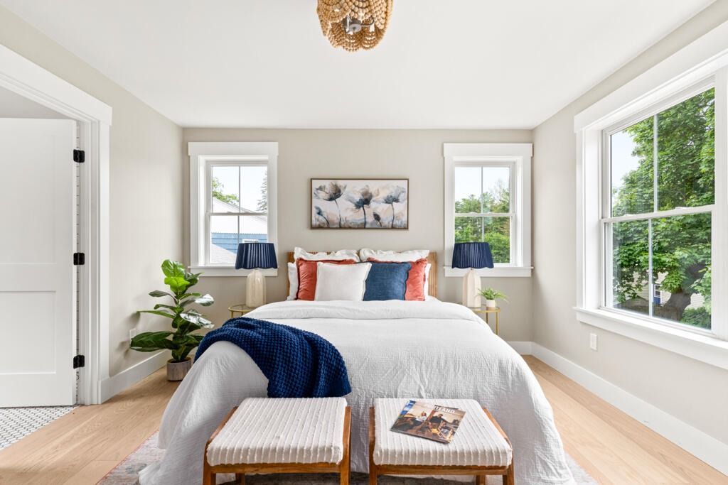Bright bedroom with a neatly made bed, blue throw blanket, and large windows on both sides.