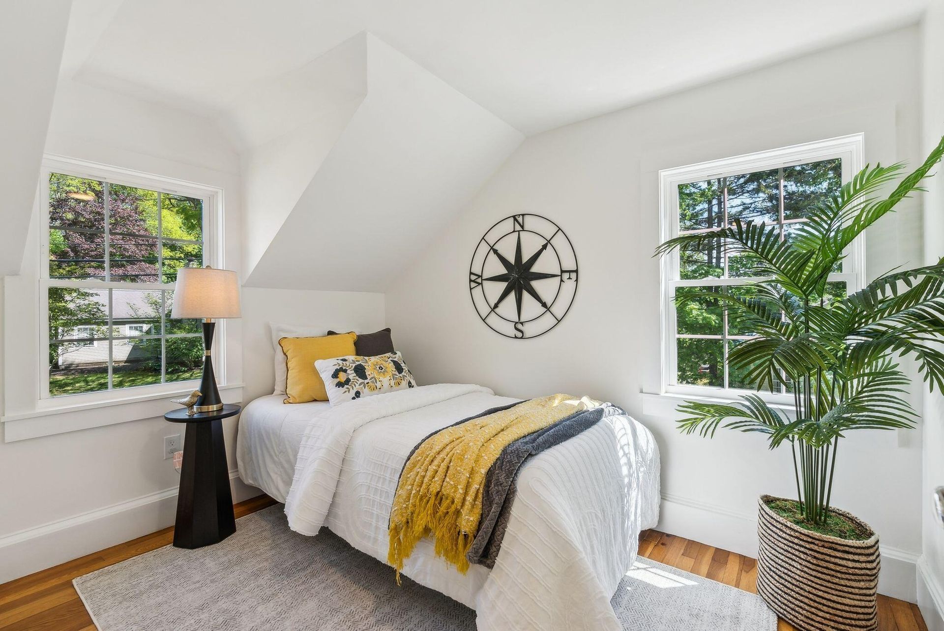 Bright white bedroom with bed, black wall clock, two windows, and a tall potted plant