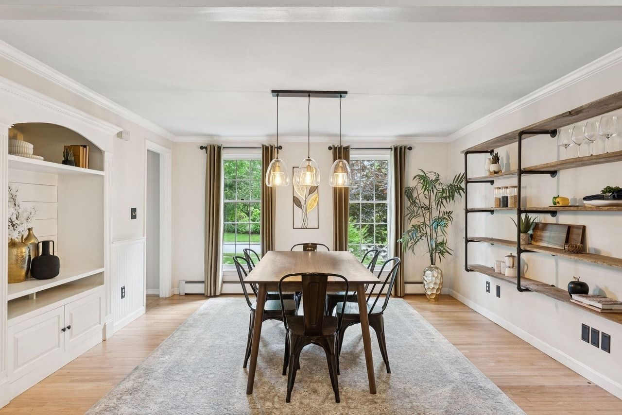 Bright dining room with wooden table, woven chairs, pendant lights, and built-in shelves by large windows