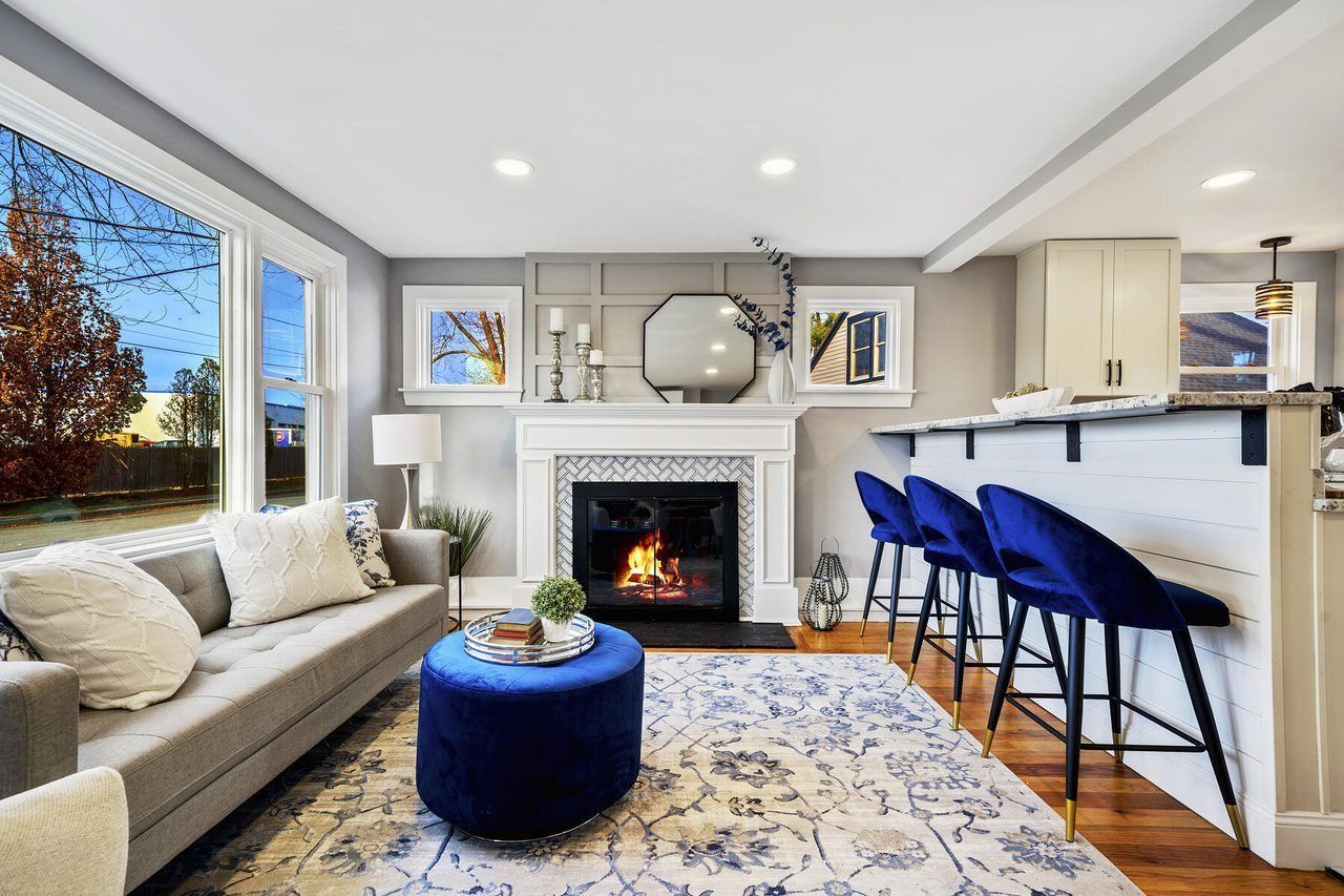 Bright living room with beige sofa, blue stools, fireplace, and large window view