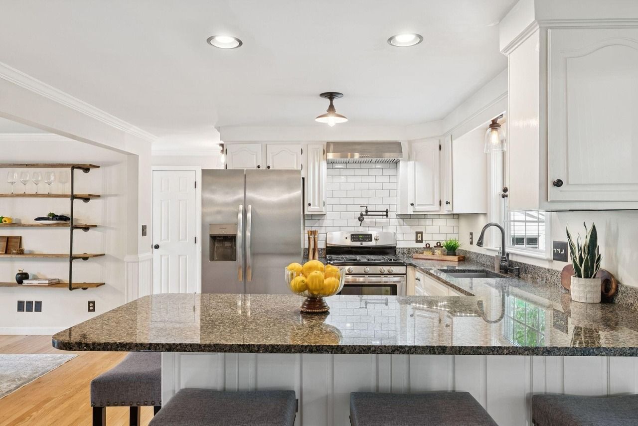 Bright modern kitchen with white cabinets, stainless steel appliances, and a granite island with fruit bowl.