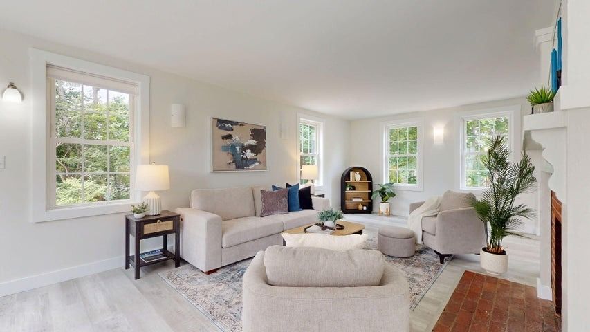 Bright living room with light sofas, windows, a lamp, and a brick fireplace.