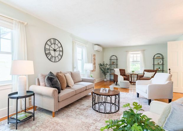 Bright, airy living room with beige sofa, white chairs, round coffee table, and large wall clock