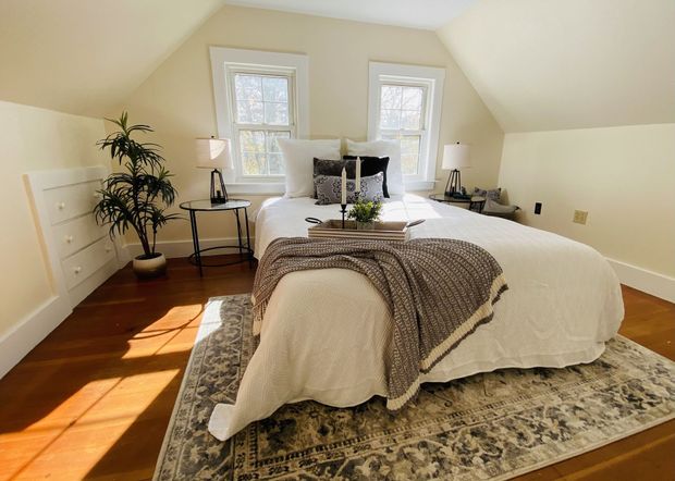 Bright bedroom with a neatly made white bed, patterned rug, and sunlight streaming through two windows.