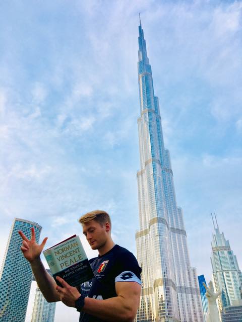 Xander Clemens in Dubai in front of the Burj Khalifa reading the book The Positive Principle Today by Norman Vincent Peale