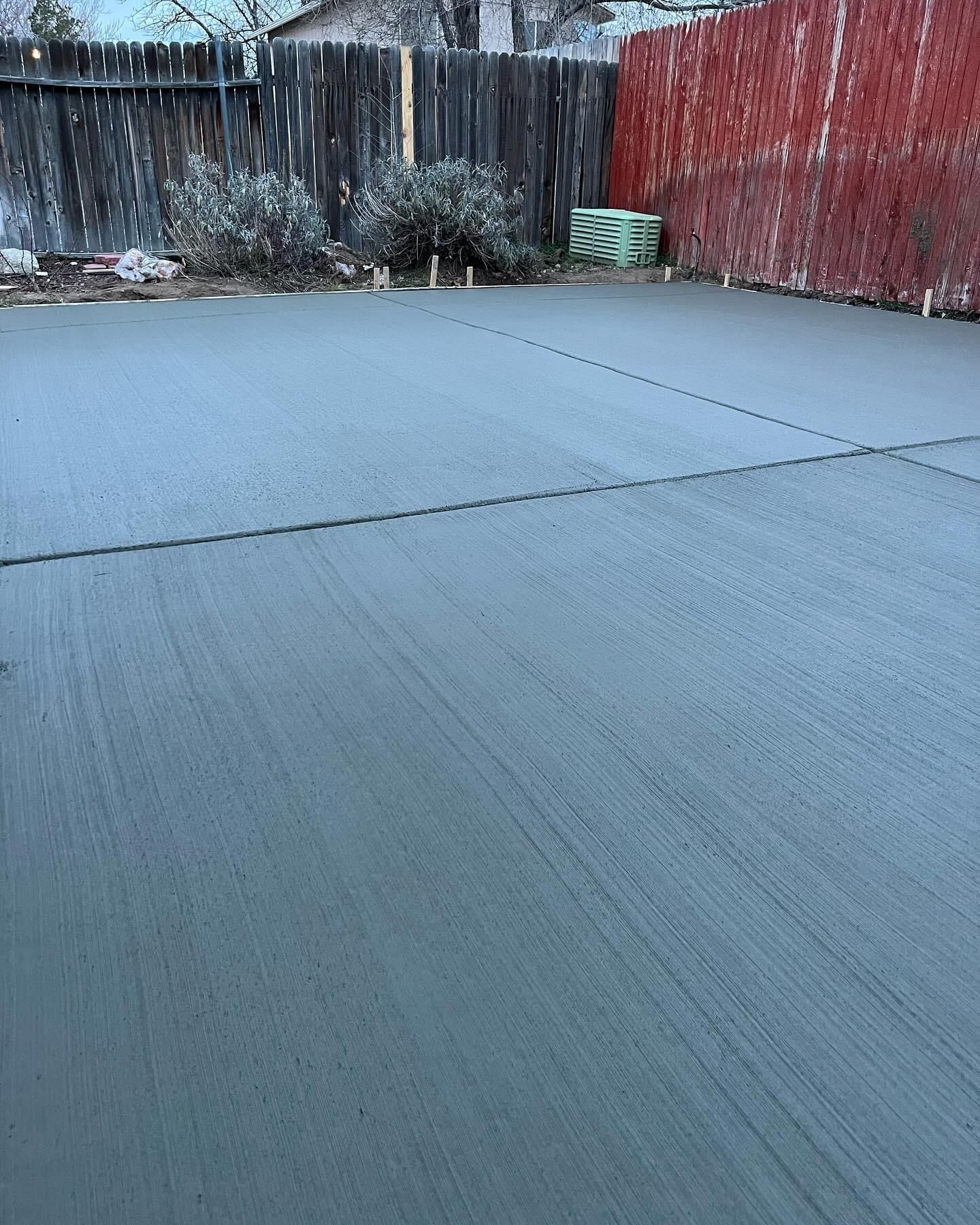 A concrete driveway with a red fence in the background.